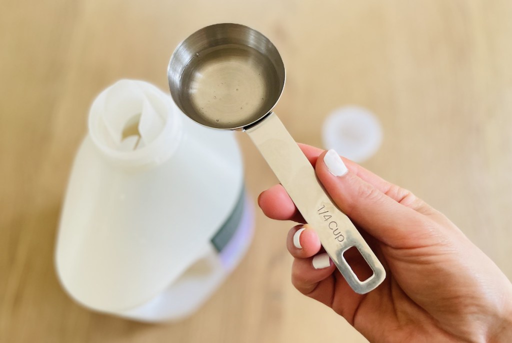 hand holding a measuring cup with laundry detergent inside