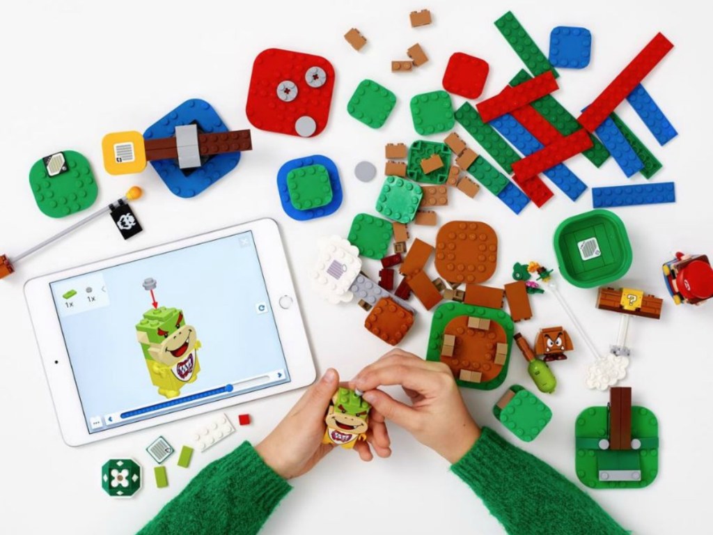 hands playing with LEGOs and a tablet on table