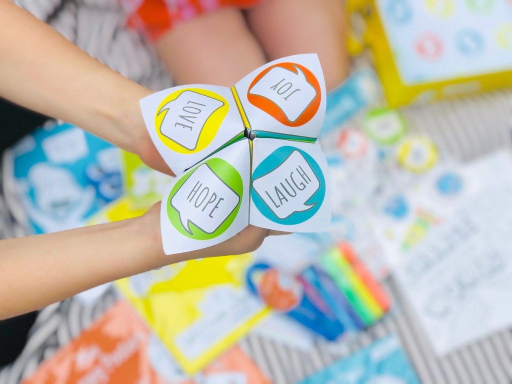 hands holding folded paper toy with words and colors on outside