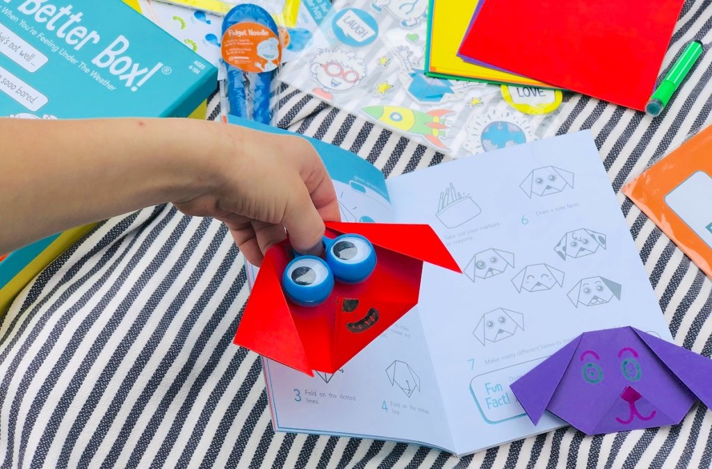 hand holding a red paper dog face with origami booklet in background