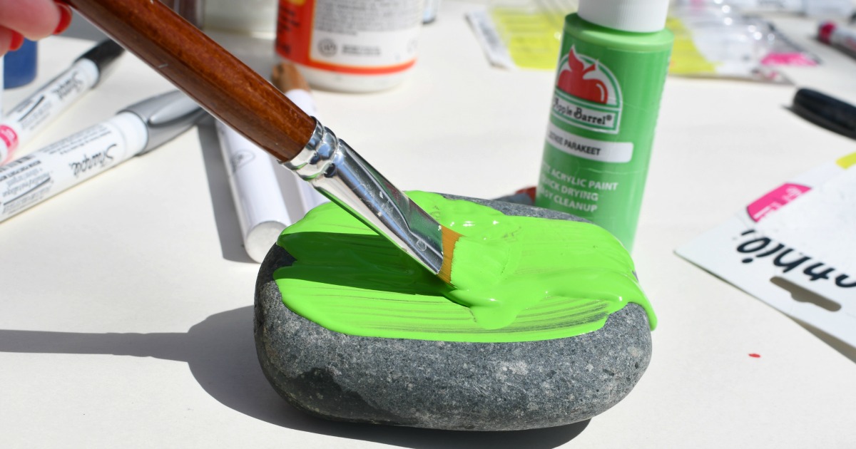paintbrush painting a rock with green paint