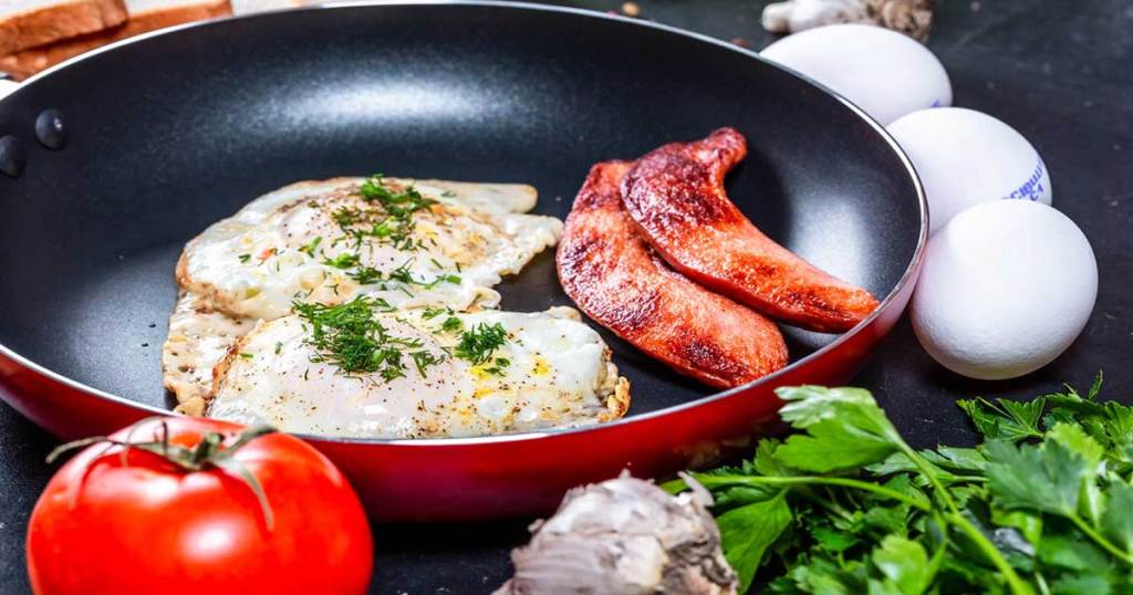 close up of a red skillet with bacon and eggs in it