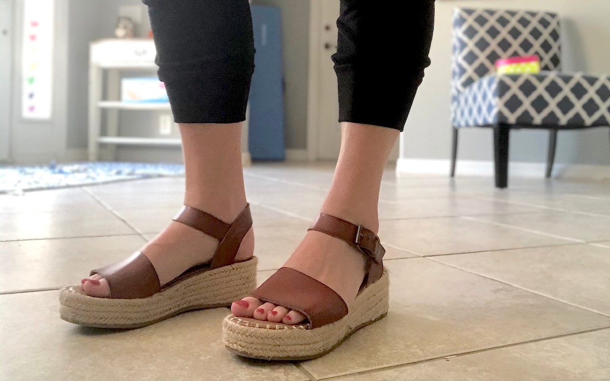 close up of feet wearing brown leather wedge sandals on tile floor