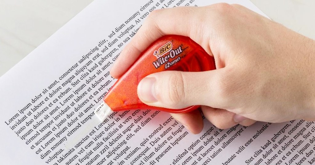 person holding a red wite-out tape dispenser over a printed document