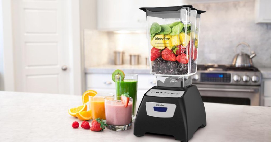 Blendtec Classic 570 Blender on counter with fruit inside of it and smoothies to the side