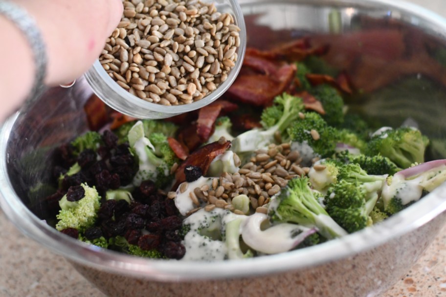 adding sunflower seeds to broccoli salad with bacon