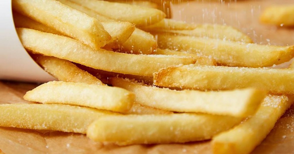 fries spilled out onto wooden counter with sea salt being sprinkled on them