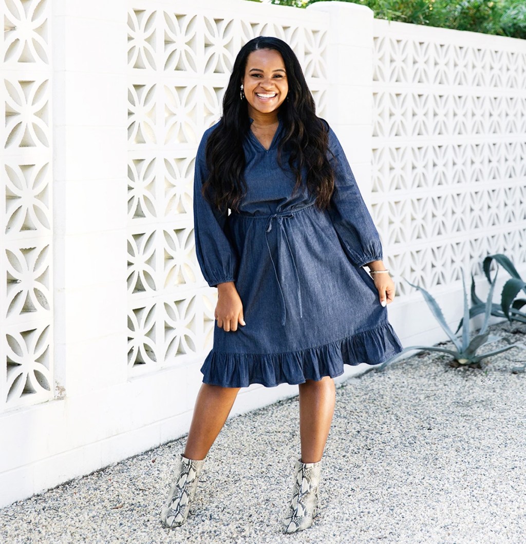 woman in ruffle hem denim dress with snakeskin booties outside near white stone wall