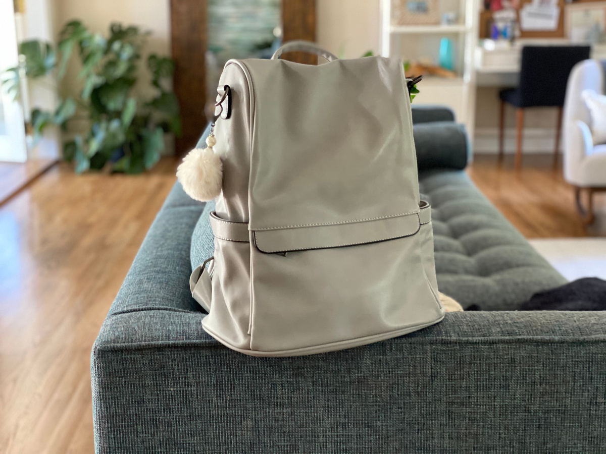 silver backpack purse sitting atop of blue/grey couch