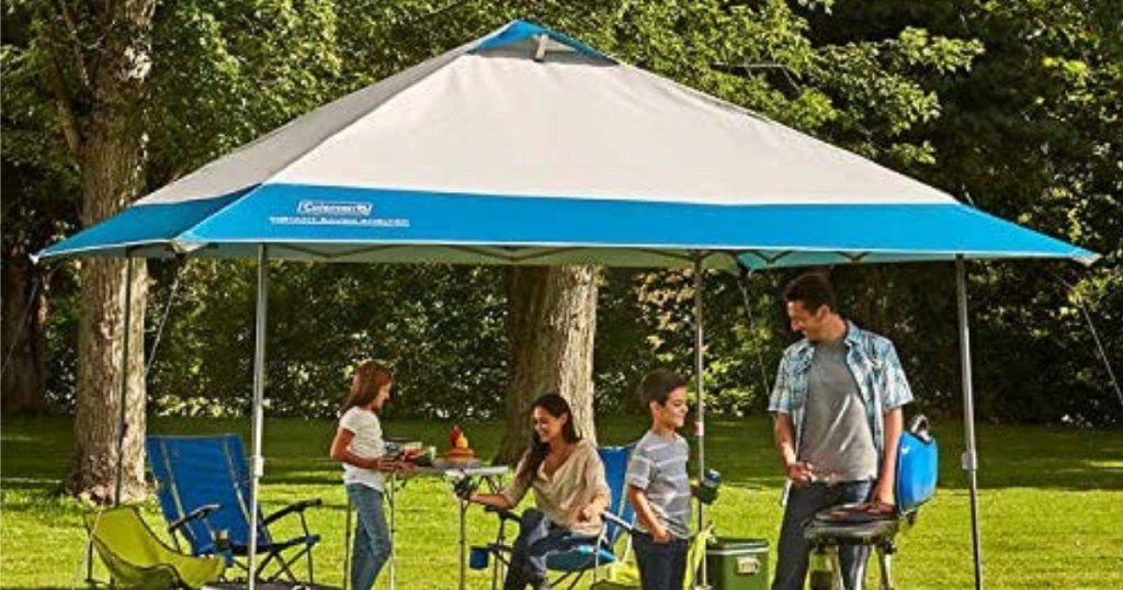 family underneath tan and blue colored Coleman 13' x 13' Instant Eaved Shelter outside