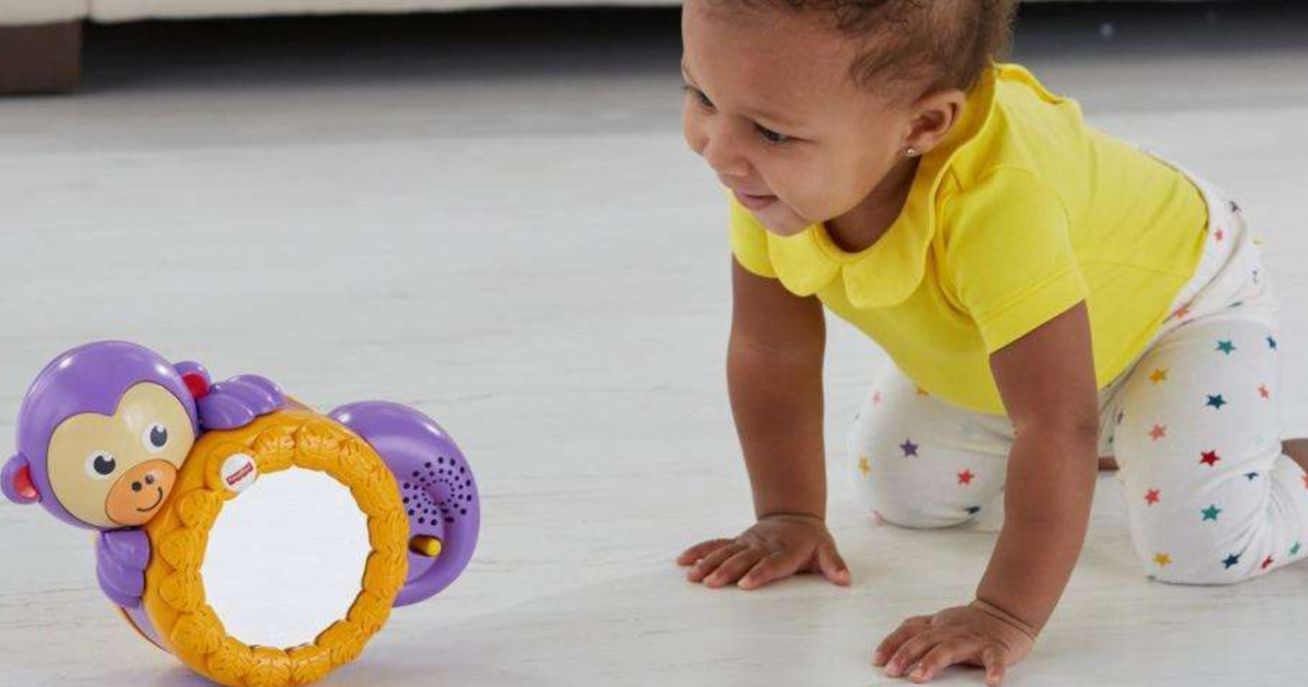 baby wearing a yellow top crawling on the floor behind fisher price monkey toy 