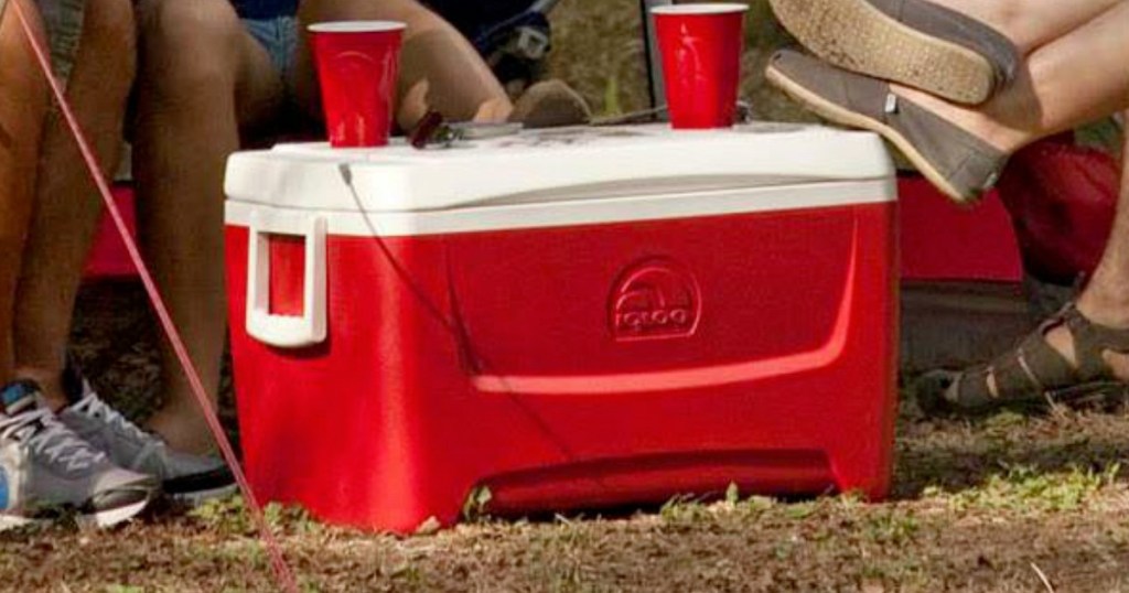 red igloo cooler with white lid and handles sitting outside with two red cups sitting on top of lid