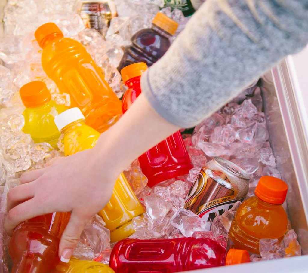 person reaching into cooler filled with ice and various soda and bottled drinks