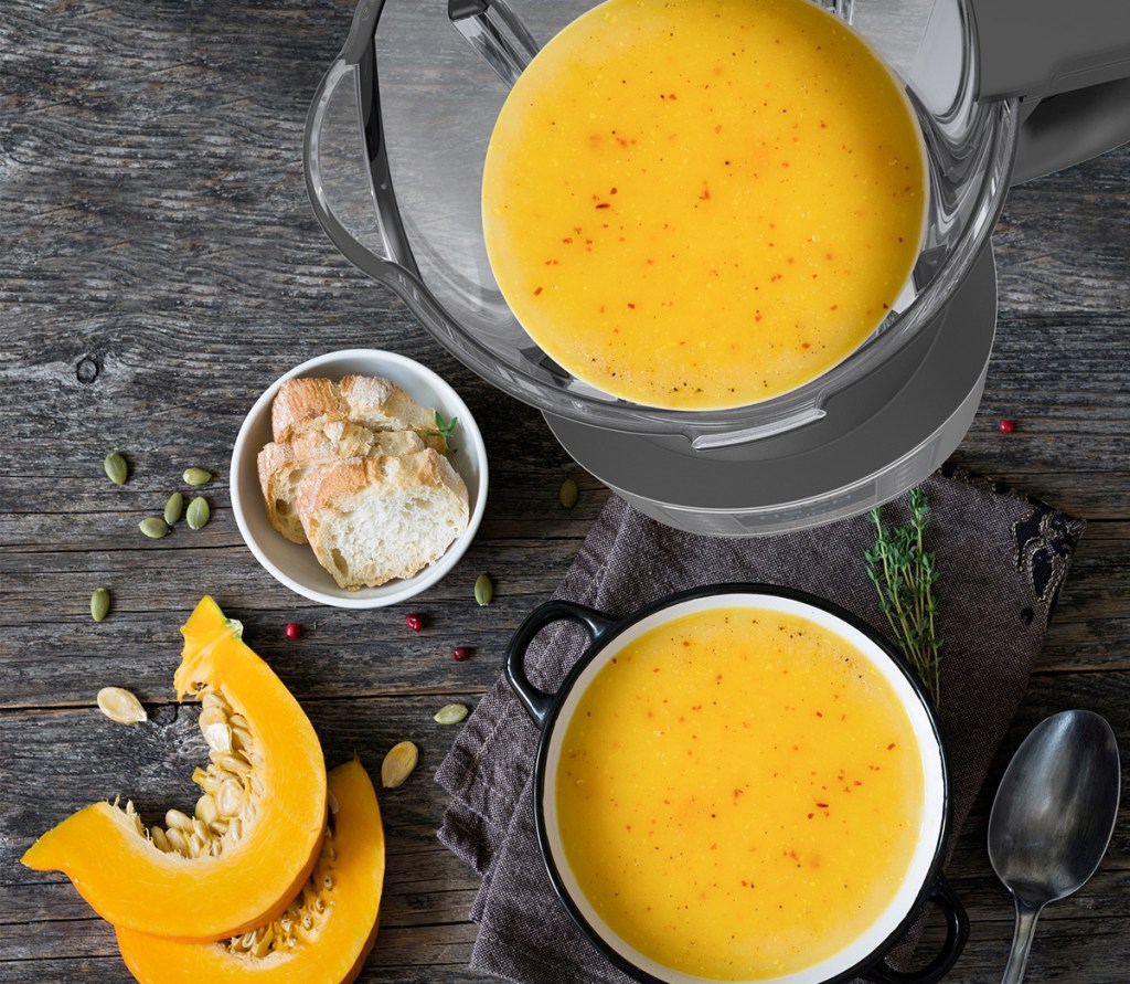 blender making butternut squash soup with pieces of squash, bowls and spoons around it