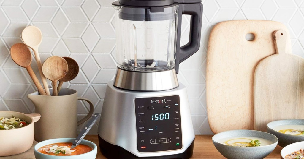 stainless steel and black blender on kitchen counter near bowls of soup, utensils, and cutting boards