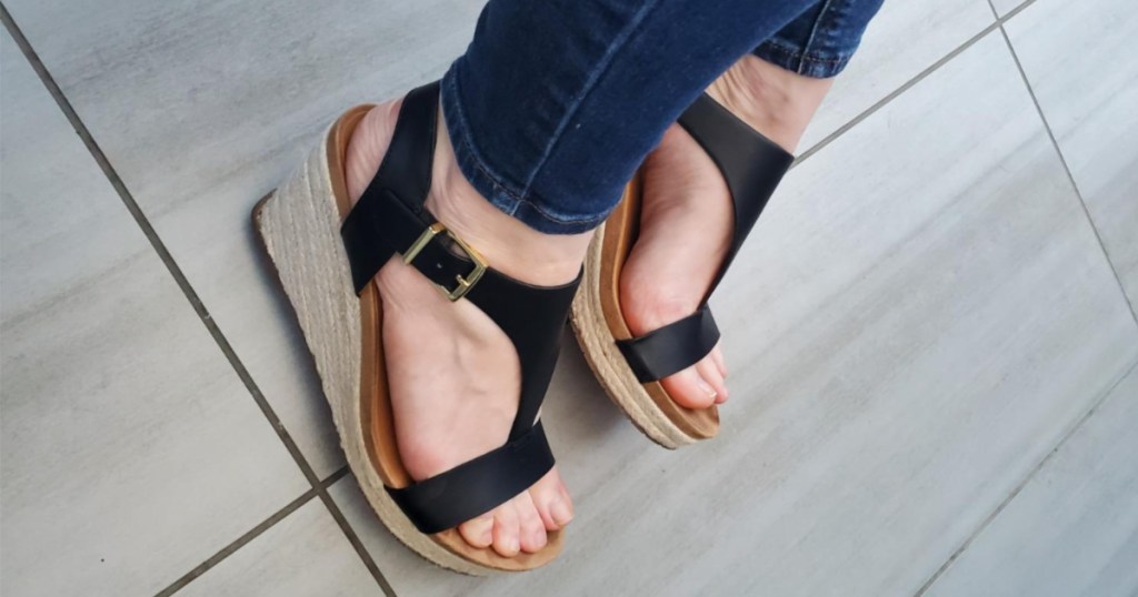 dark jeans and feet wearing black open-toed sandals with side buckle strap and wedge heel