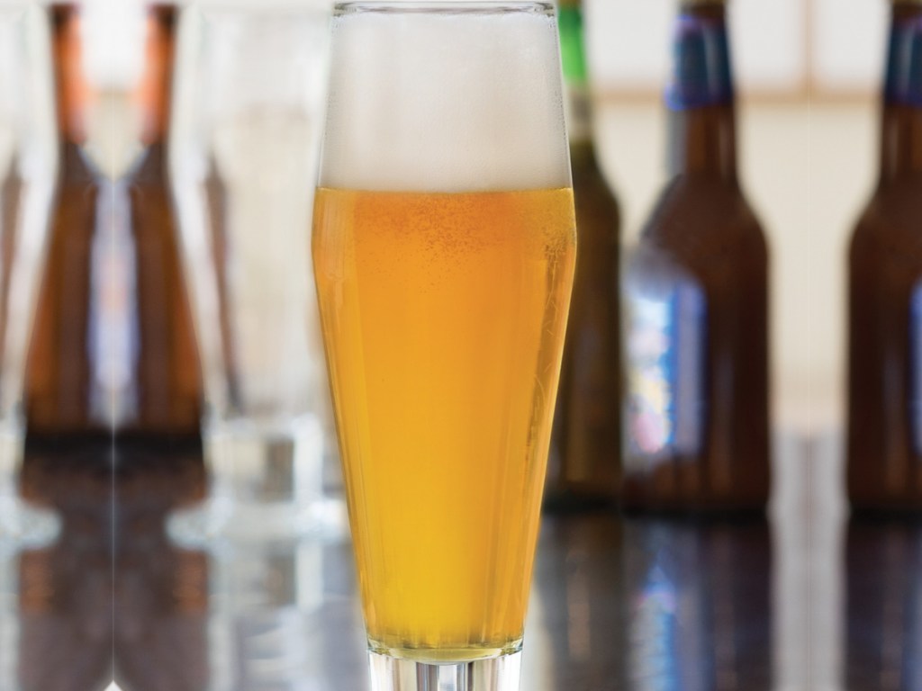 tall pilsner glass filled with beer surrounded by beer bottles