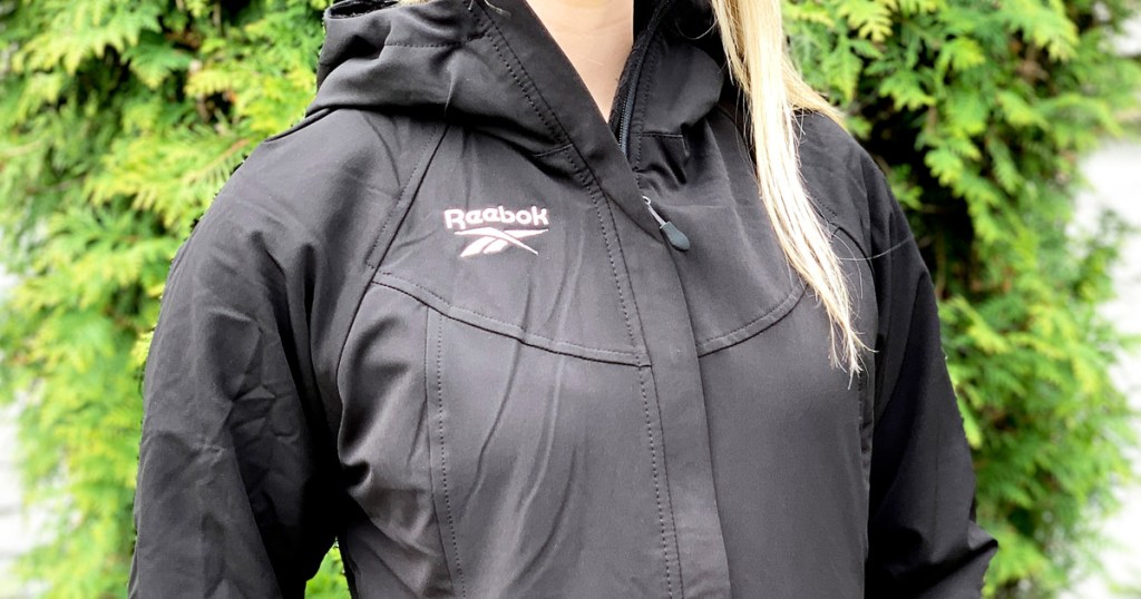 woman with blonde hair wearing black reebok jacket outside in front of greenery