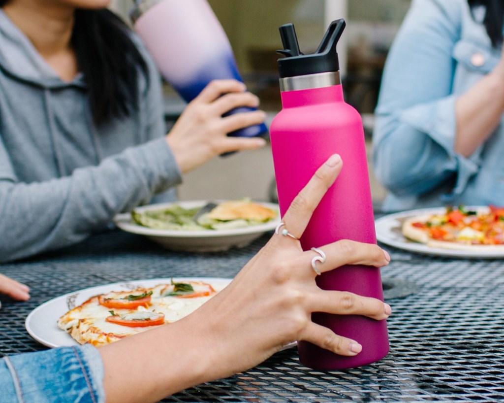 person sitting at black patio table holding a dark pink ombre water bottle