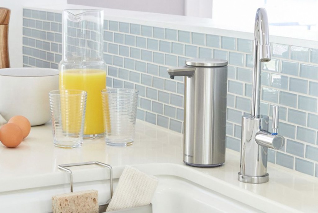stainless steel colored soap dispenser next to chrome faucet and sink with light blue backsplash