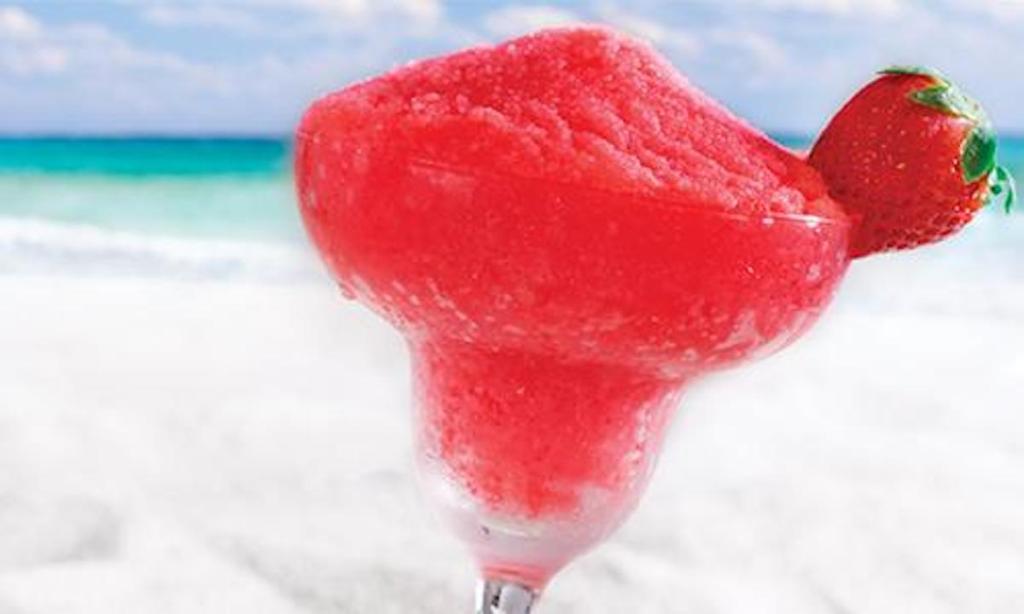 bright pink red cocktail drink with strawberry garnish and beach in background