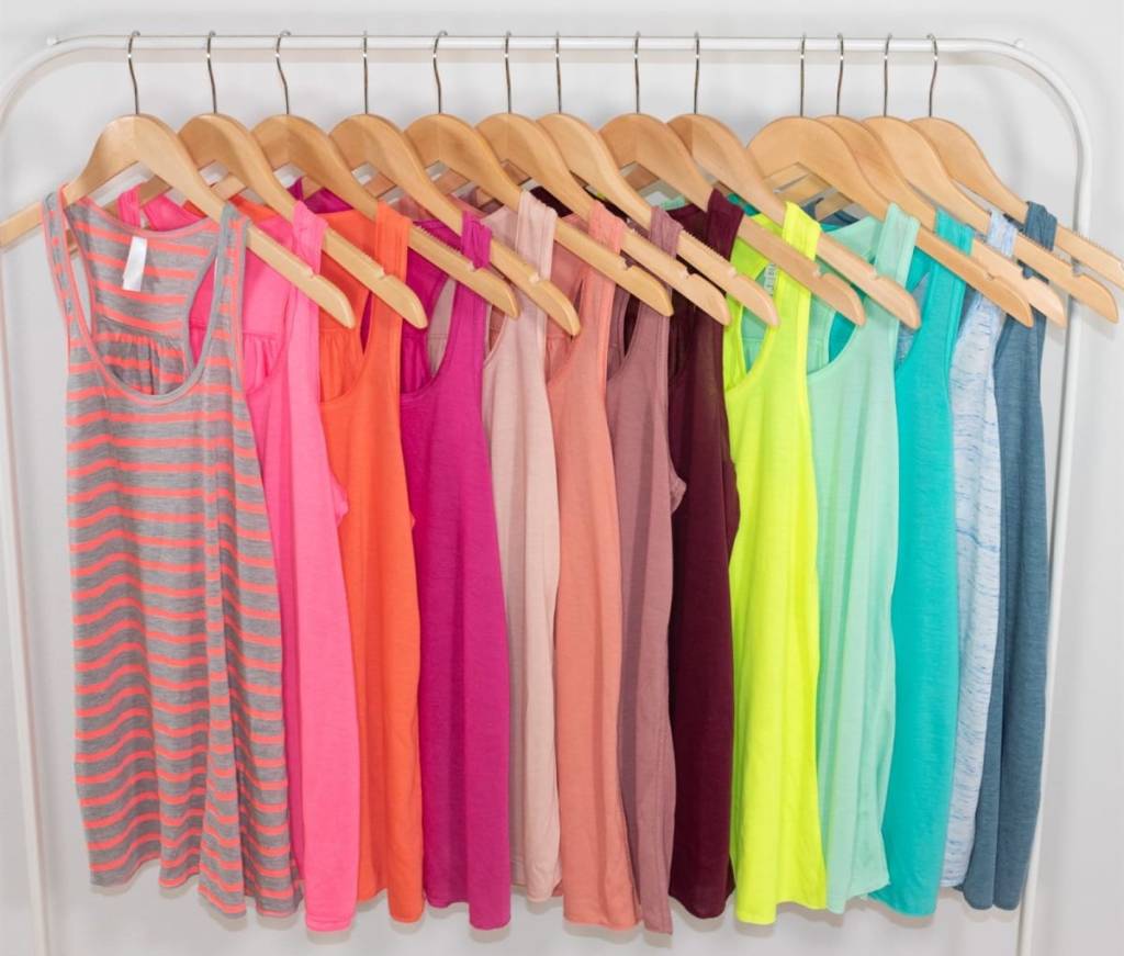 multiple tank tops in a wide variety of bright colors handing on wooden hangers