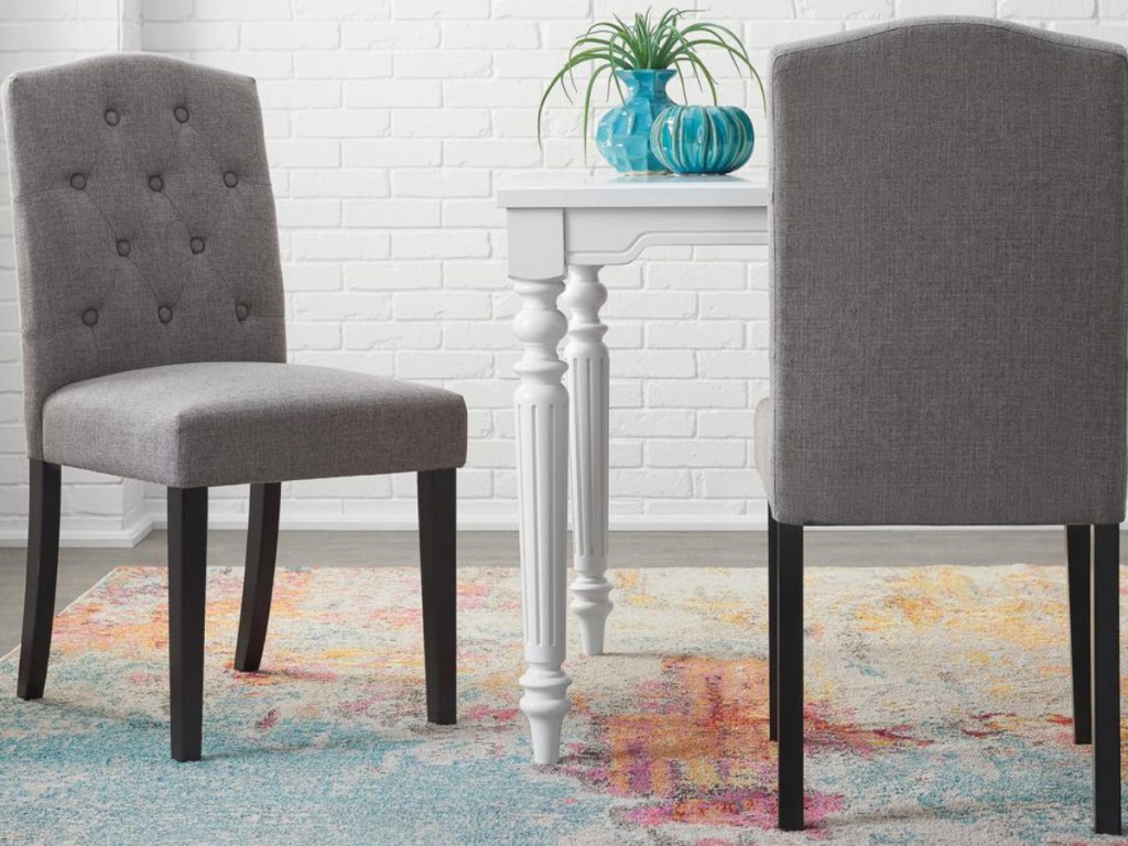 2 grey tufted dining chairs sitting next to a white table with a plant