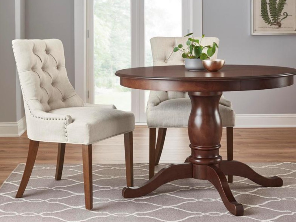 2 white tufted dining chairs next to a round brown kitchen table