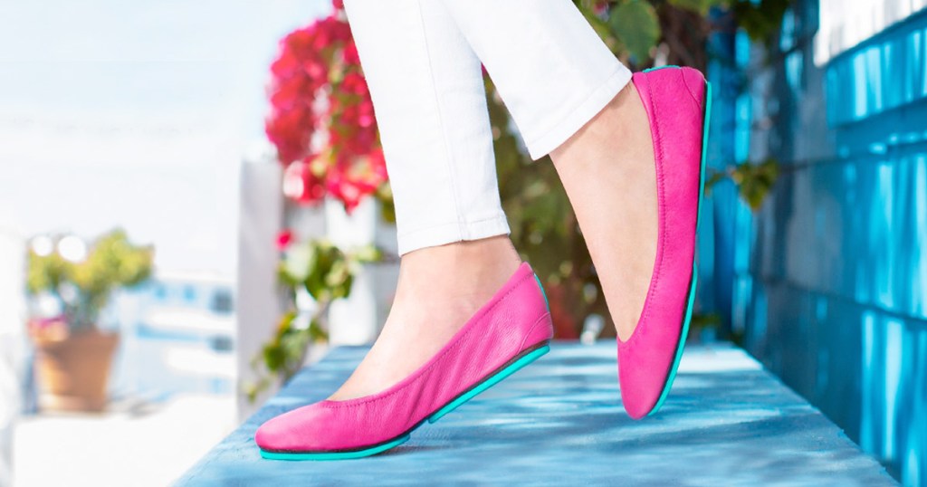 woman wearing white pants and bright pink ballet flats standing on blue bench