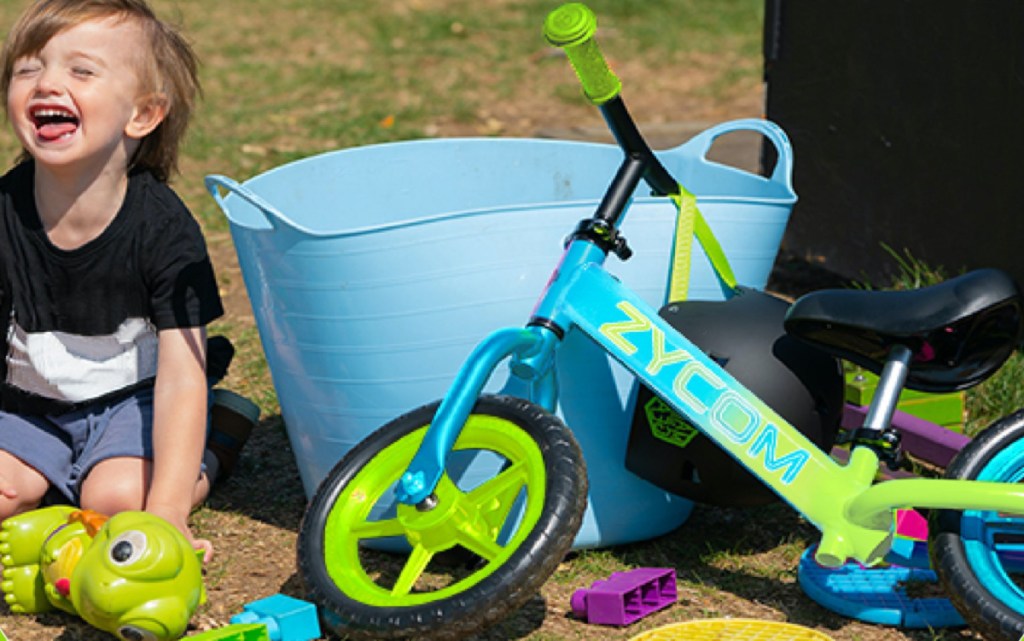 boy in grass next to toys and green and blue bike leaning against large blue bucket
