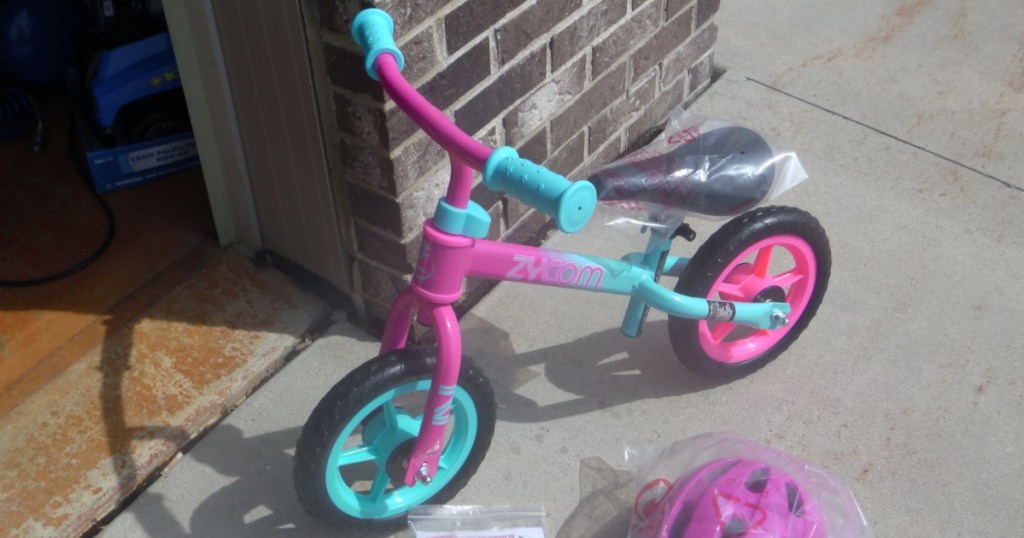 small kids pink and blue bike against brick wall outside with pink helmet in plastic on ground