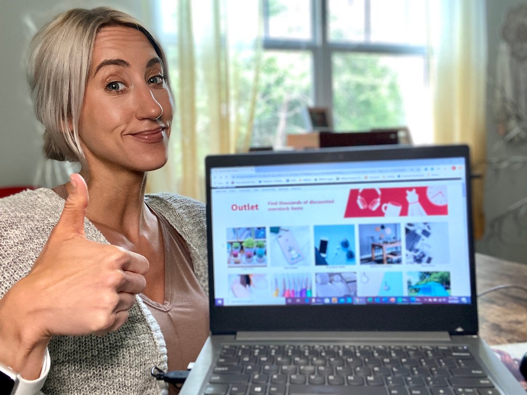 woman holding computer with Amazon outlet on screen and doing a thumbs up