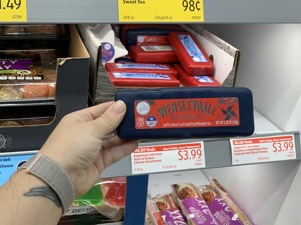 hand holding a block of cheese in blue wax in front of a store display