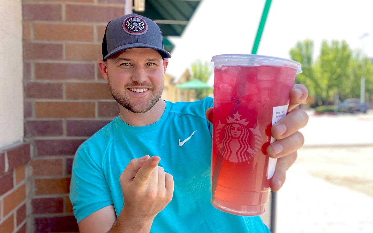 man holding a plastic starbucks cup with red drink inside