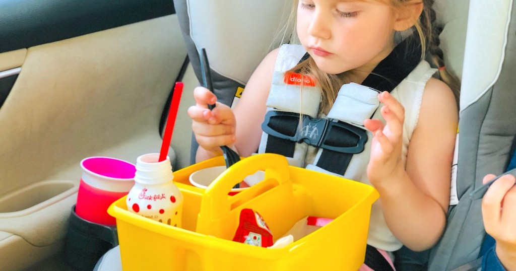 girl sitting in carseat with yellow caddy on lap filled with fast food