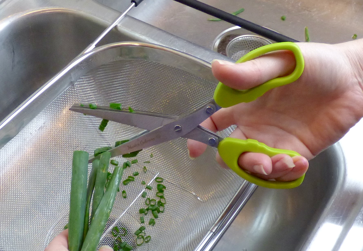 hand holding a pair of multi blade scissors cutting scallions