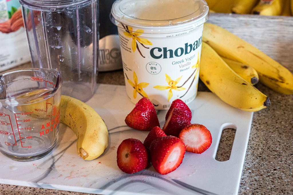 sliced strawberries, greek yogurt, and bananas on a cutting board