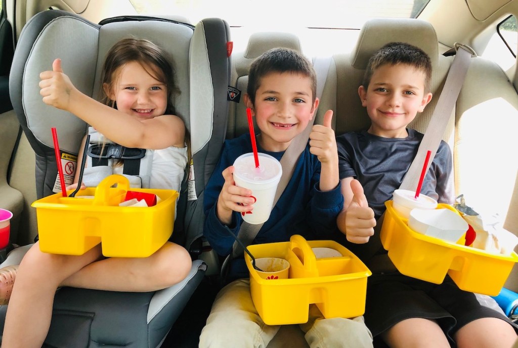 three kids sitting in car with yellow classroom caddies and fast food on lap