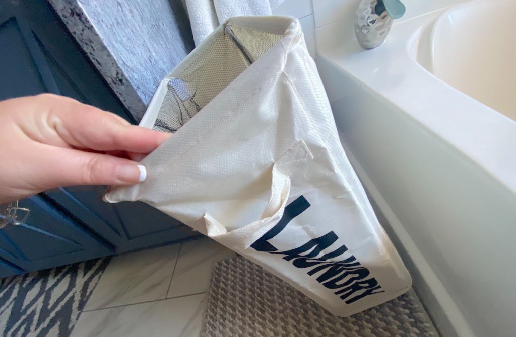 hand holding a laundry basket next to bathtub