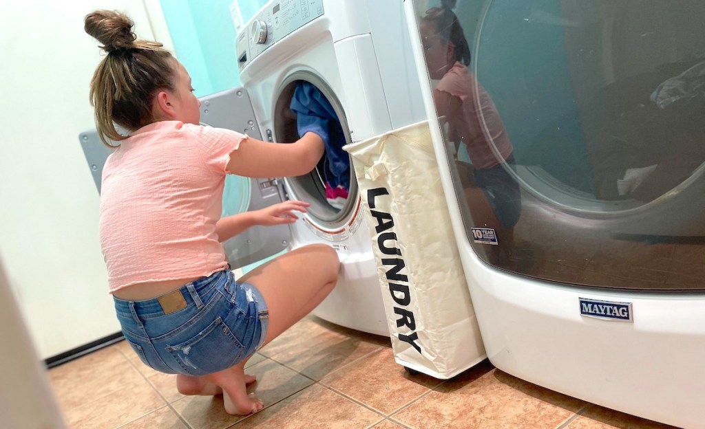 girl loading clothes into washing machine with laundry basket on floor