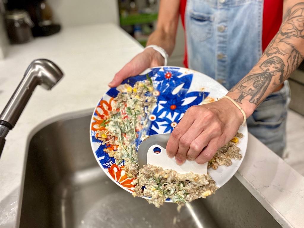 woman removing leftovers from plate with dish squeegee