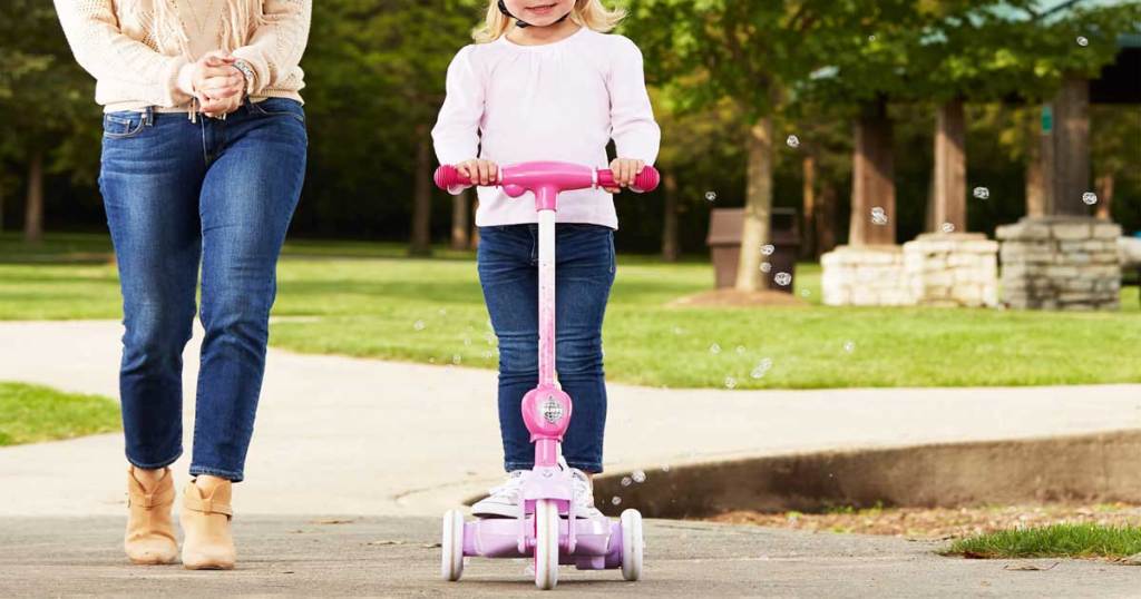 little girl riding disney scooter with bubbles and mom standing to the side