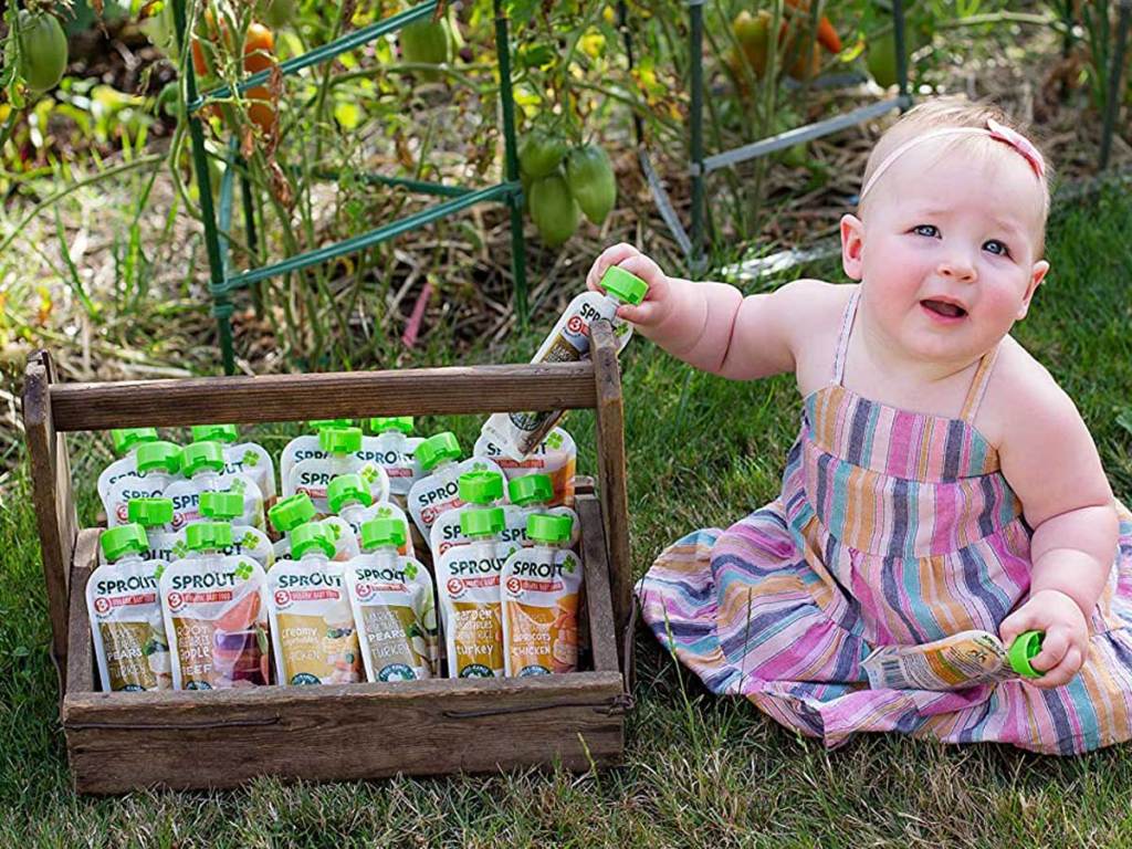 baby girls in grass next to container with baby food pouches