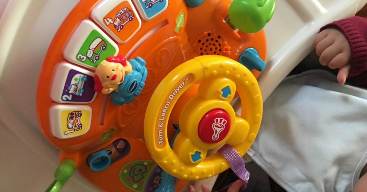 small child sitting by toy with steering wheel