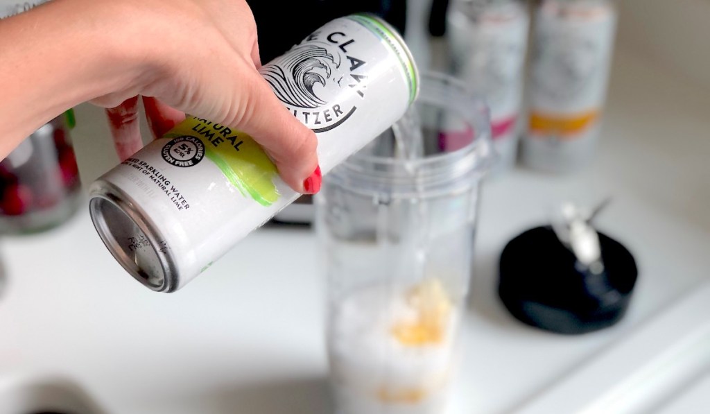 hand holding white claw can pouring into blending cup