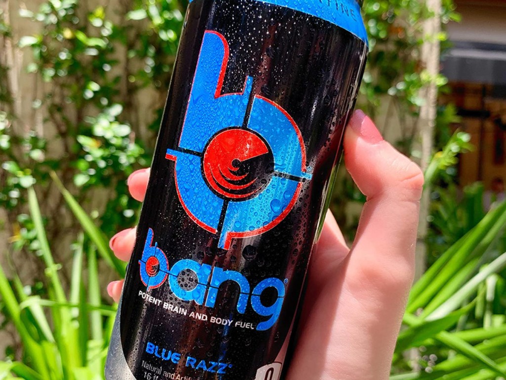 woman's hand holding can of blue razz energy drink with foliage in backgroun