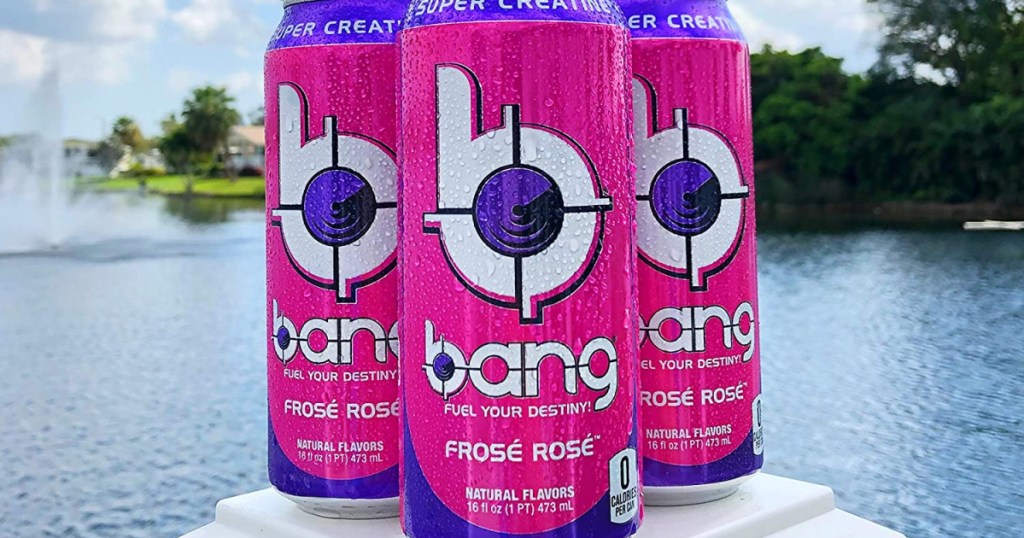three cans of pink energy drinks with lake in background
