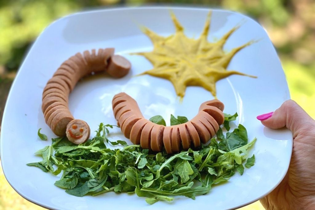 A hand holding a plate with lettuce and hot dogs