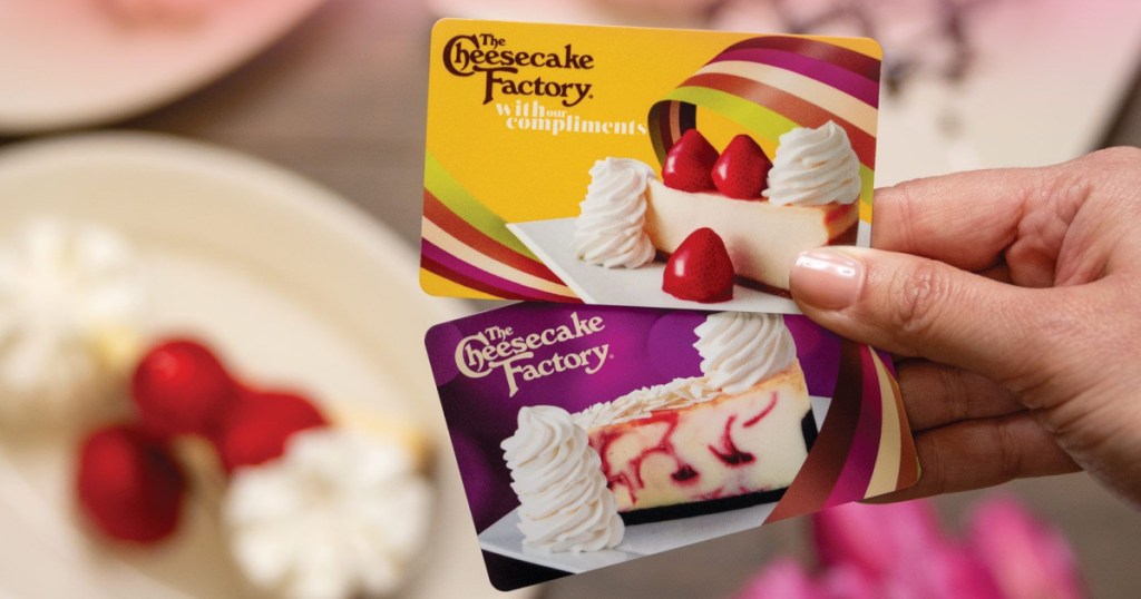 woman's hand holding two Cheesecake Factory gift cards with plates of cheesecake in background