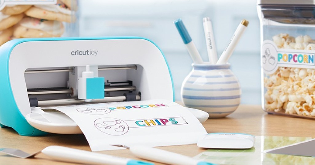Cricut Joy printing out a colorful sheet of paper next to markers and popcorn snacks